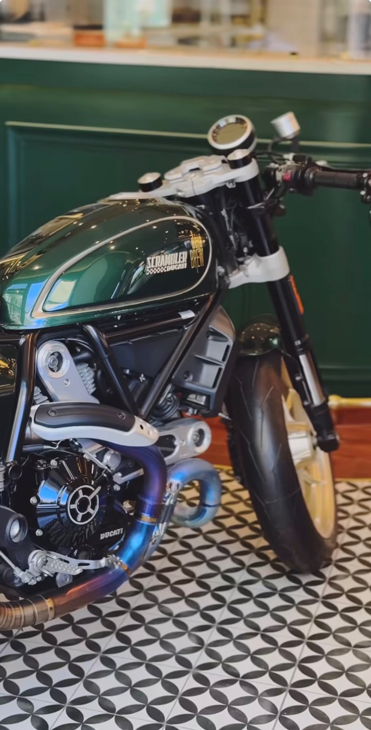 Deja Brew branded Ducati Scrambler parked on patterned tile inside the café